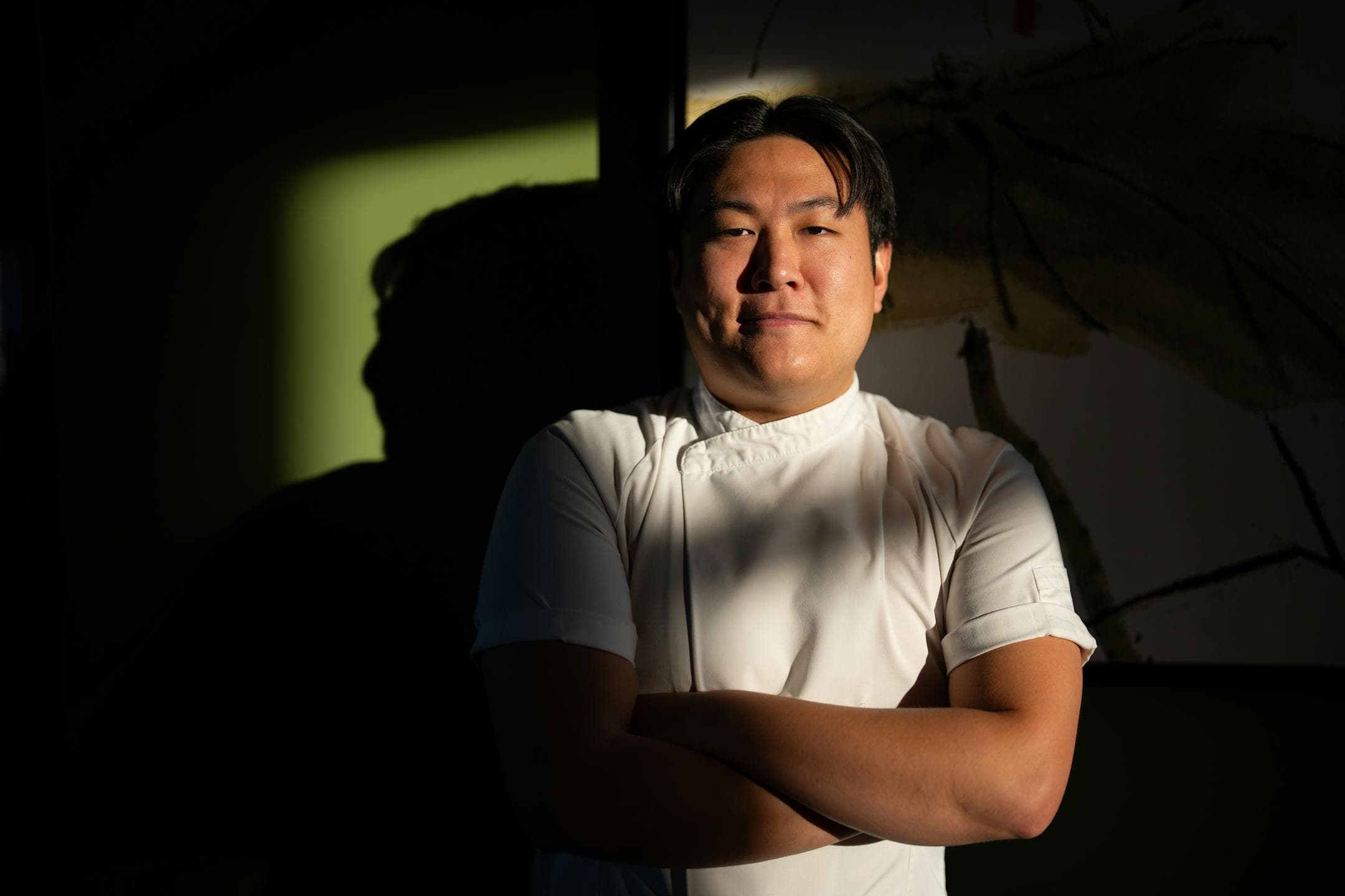 Khue's Kitchen chef-owner Eric Pham posing confidently in his white chef's coat with dramatic lighting.