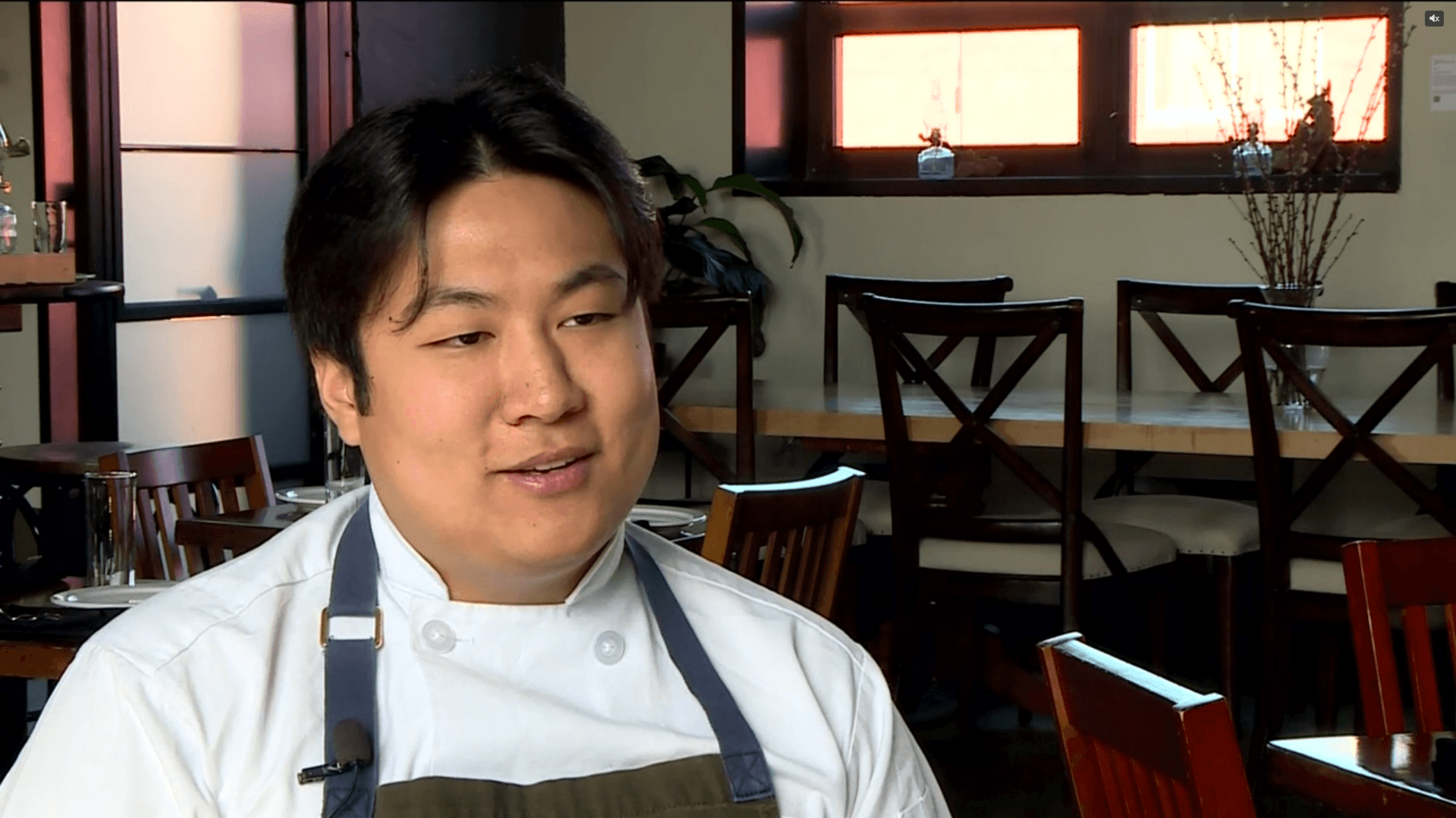 Chef Eric Pham, wearing a white chef's coat and apron, seated inside the dining room of Khue's Kitchen while discussing the reopening after a devastating fire.