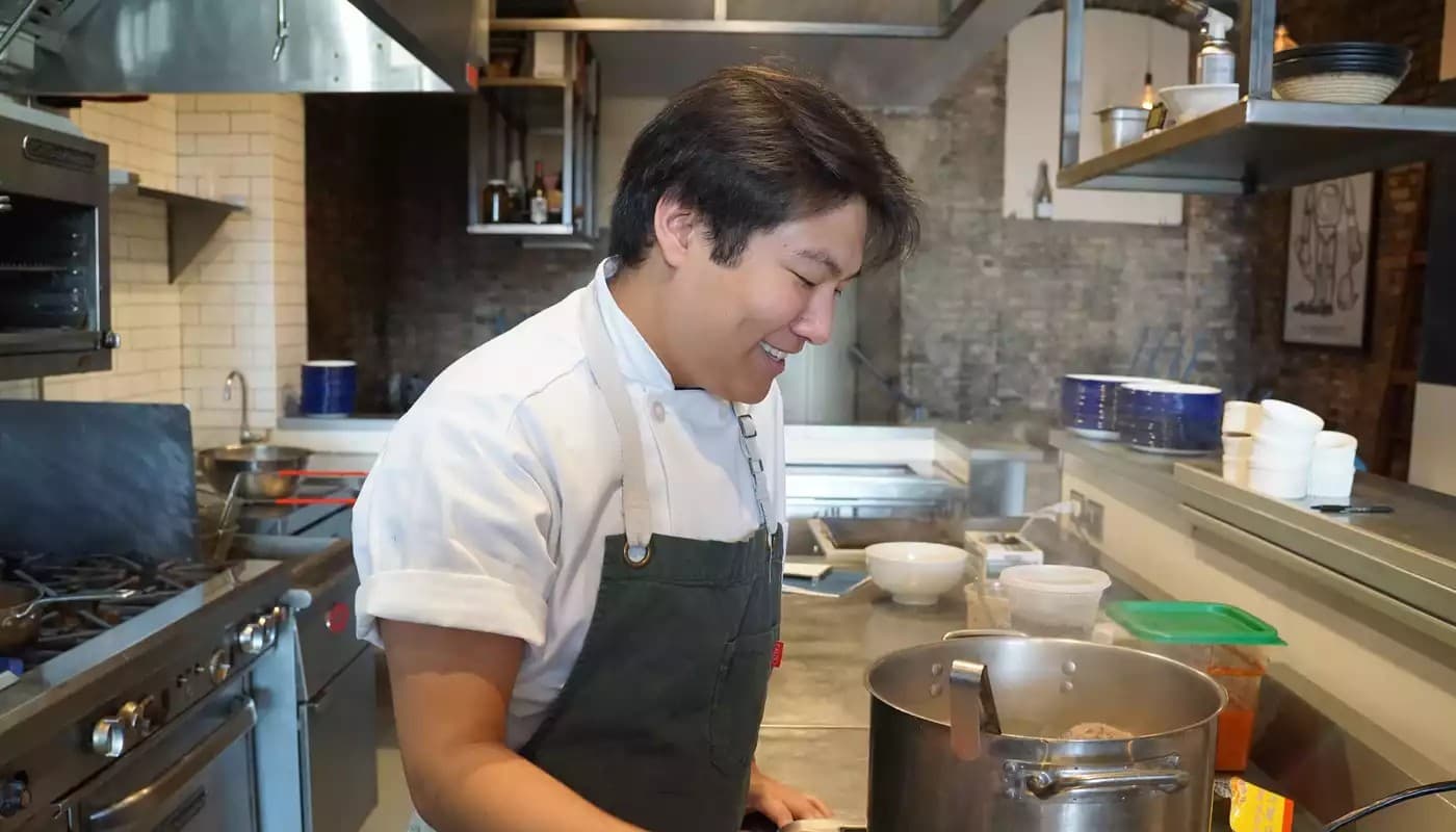 Chef Eric Pham, owner of Khue's Kitchen, smiling while cooking in a professional kitchen.