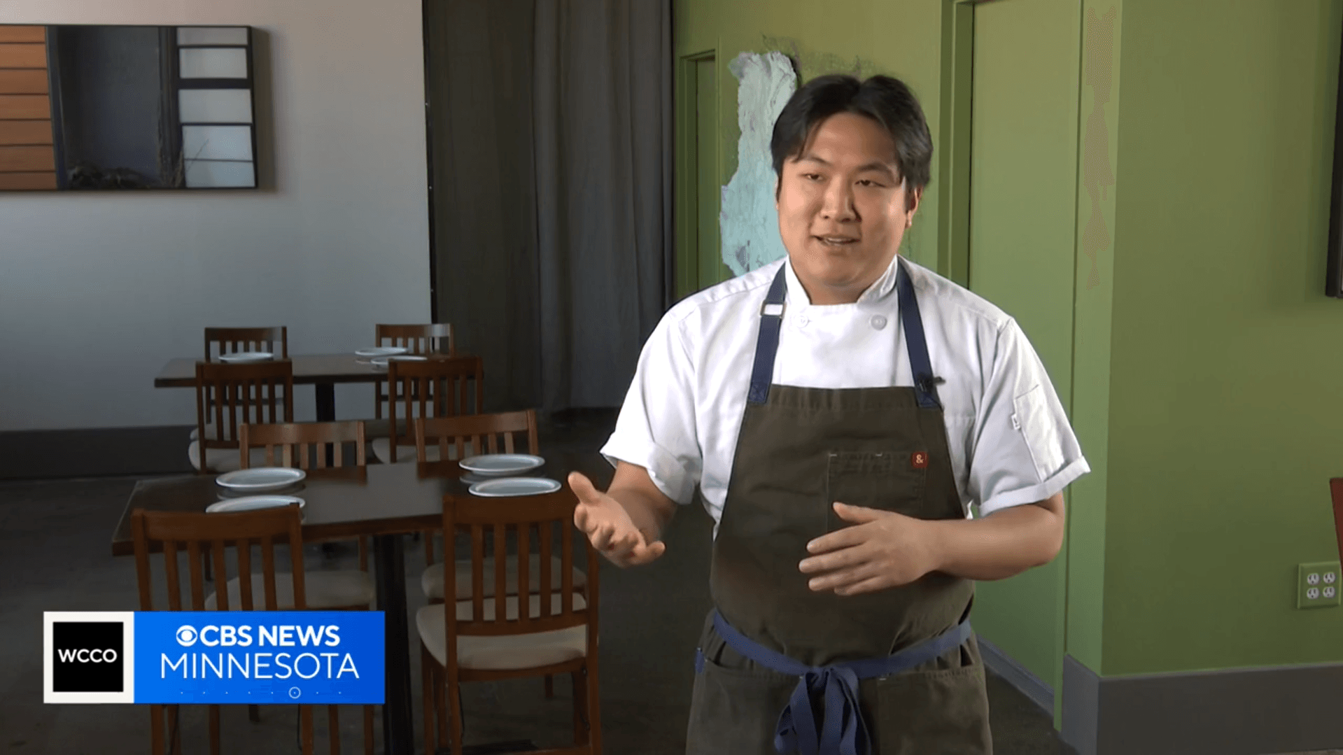 Chef Eric Pham, in a white chef's coat and apron, standing in the dining room of Khue's Kitchen and gesturing as he describes his restaurant's comeback story.
